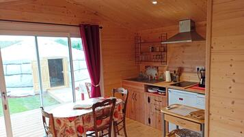 A wooden cabin with a dining area, kitchen, and sliding glass doors to a garden.