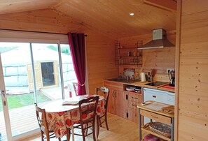 Una cabaña de madera con comedor, cocina y puertas correderas de vidrio a un jardín.