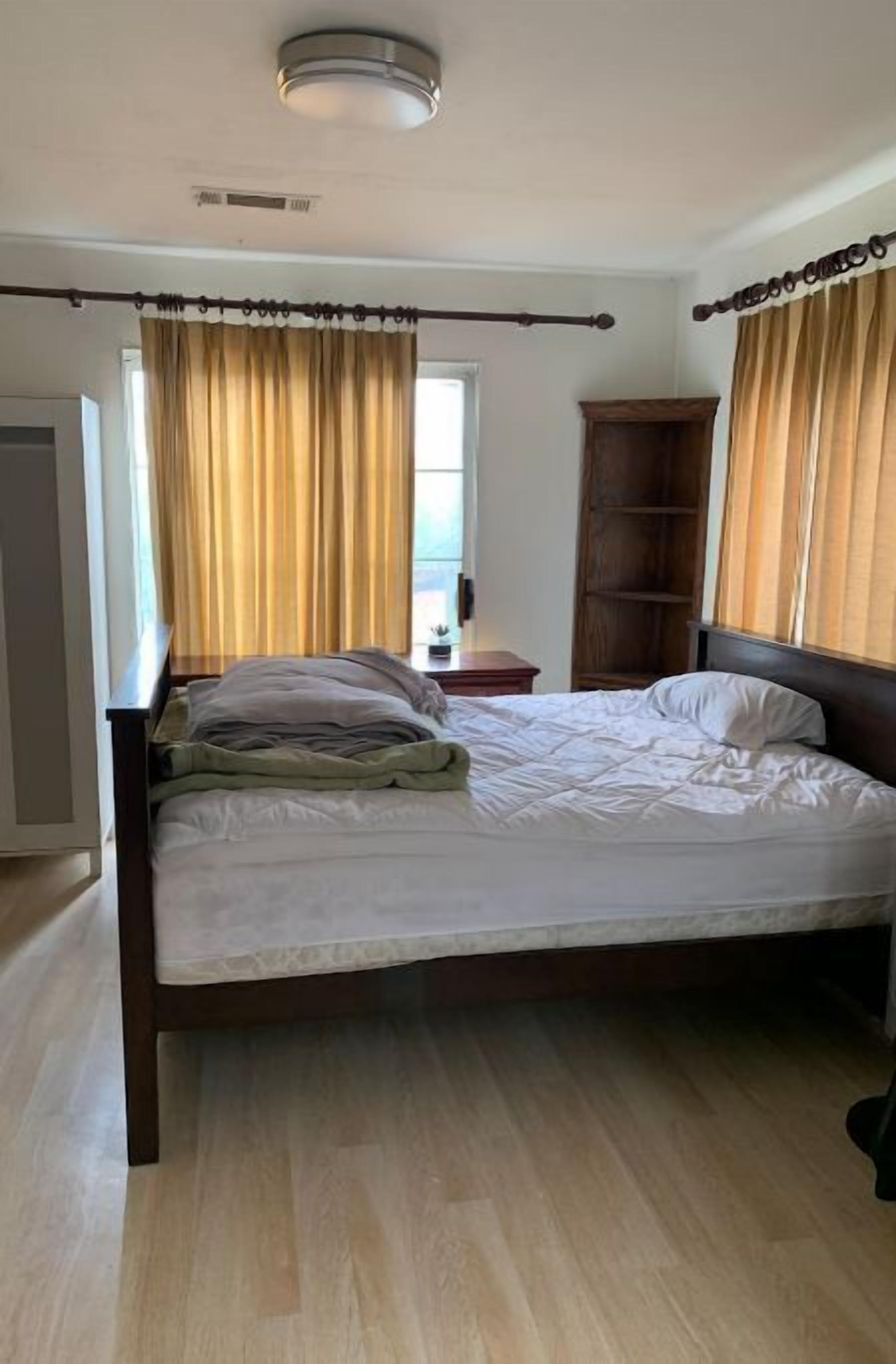 Un dormitorio con una cama de madera, una mesita de noche, un armario y una ventana con cortinas.