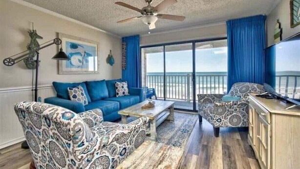 A spacious living room with a large window, a ceiling fan, and a view of the ocean. - Beachfront Oceanside Condo. Incredible view: Channel Marker  (Surfside Beach)