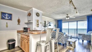 A modern kitchen with a bar area, wooden cabinets, and a view of the sea through large windows. - Beachfront Oceanside Condo. Incredible view: Channel Marker  (Surfside Beach)