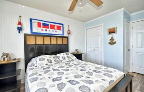 A bedroom with a bed, a headboard, a nightstand, a wall clock, and a framed picture.