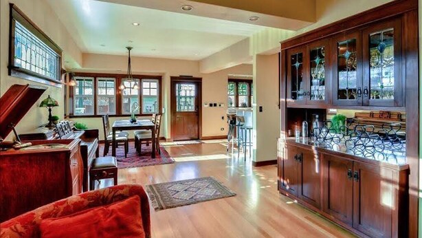 A spacious living room with a piano, a dining area, and a kitchen with wooden cabinets and a wine rack.