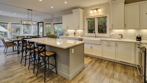 Una cocina moderna con armarios blancos, una isla central con taburetes altos y un ventanal que proporciona luz natural.