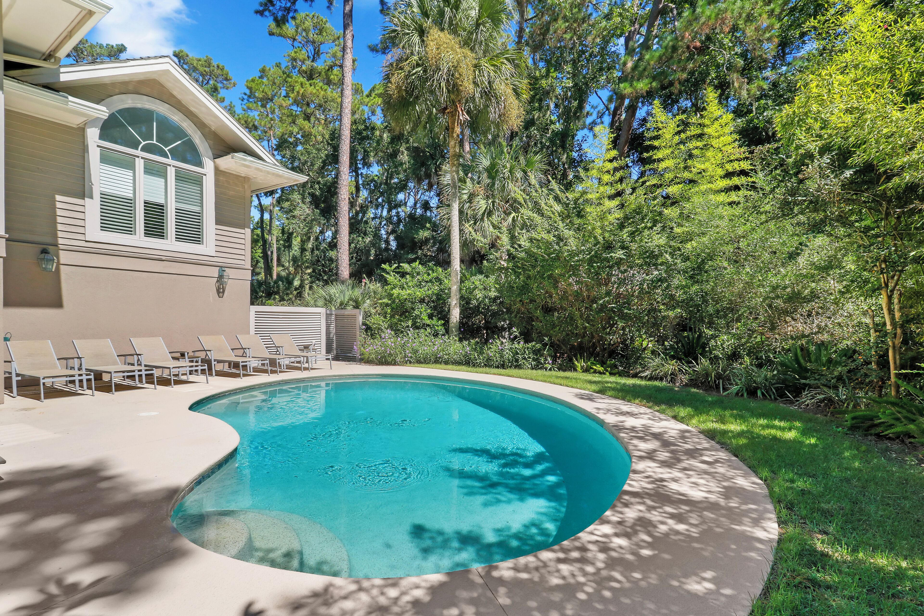 A swimming pool with a curved edge, surrounded by a concrete deck and lounge chairs.