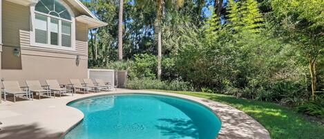A swimming pool with a curved edge, surrounded by a concrete deck and lounge chairs.