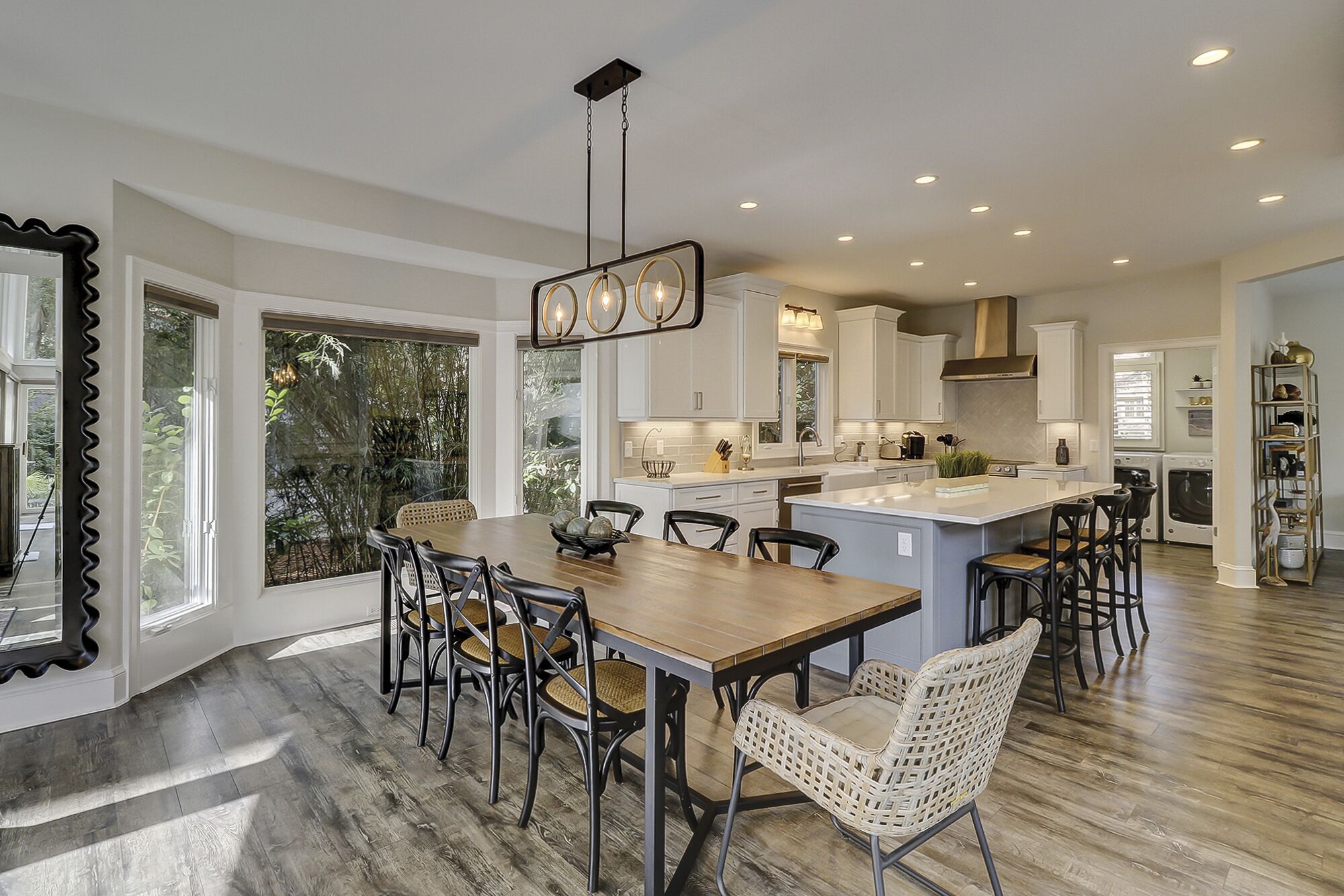 A modern kitchen with a central island, dining area with chairs, and large windows.