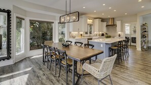 Una cocina moderna con una isla central, zona de comedor con sillas y ventanas amplias.