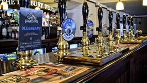 A bar with multiple beer taps, a sign for Beartown Brewery Blueberry, and a variety of liquor bottles in the background. - Hanbury Turn (Bromsgrove)
