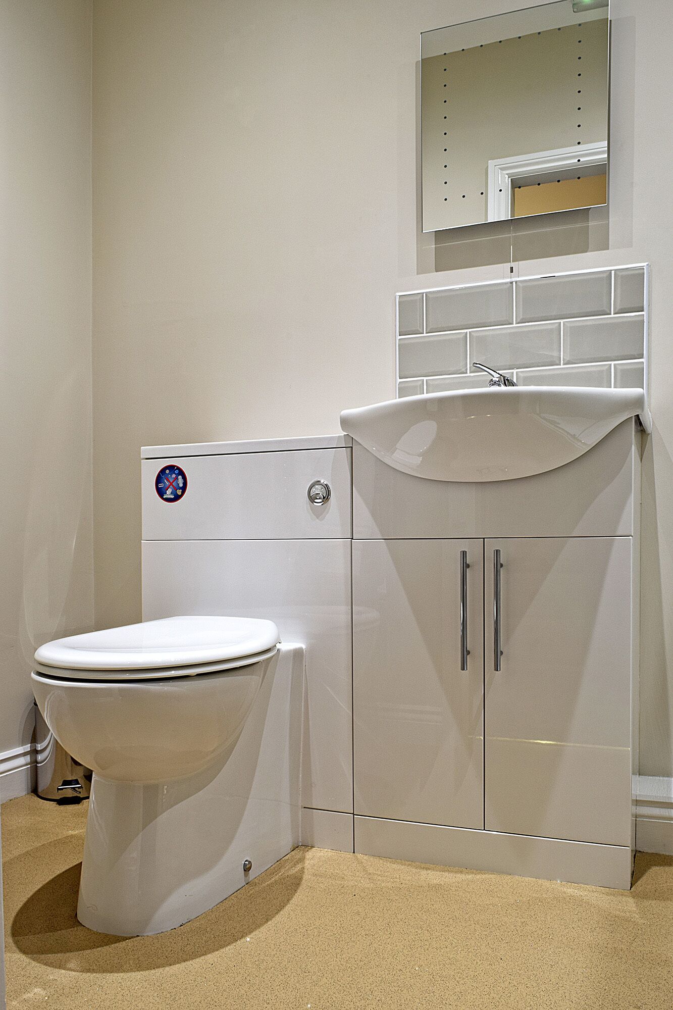 Un baño con inodoro blanco, lavamanos con espejo y mueble de dos puertas.