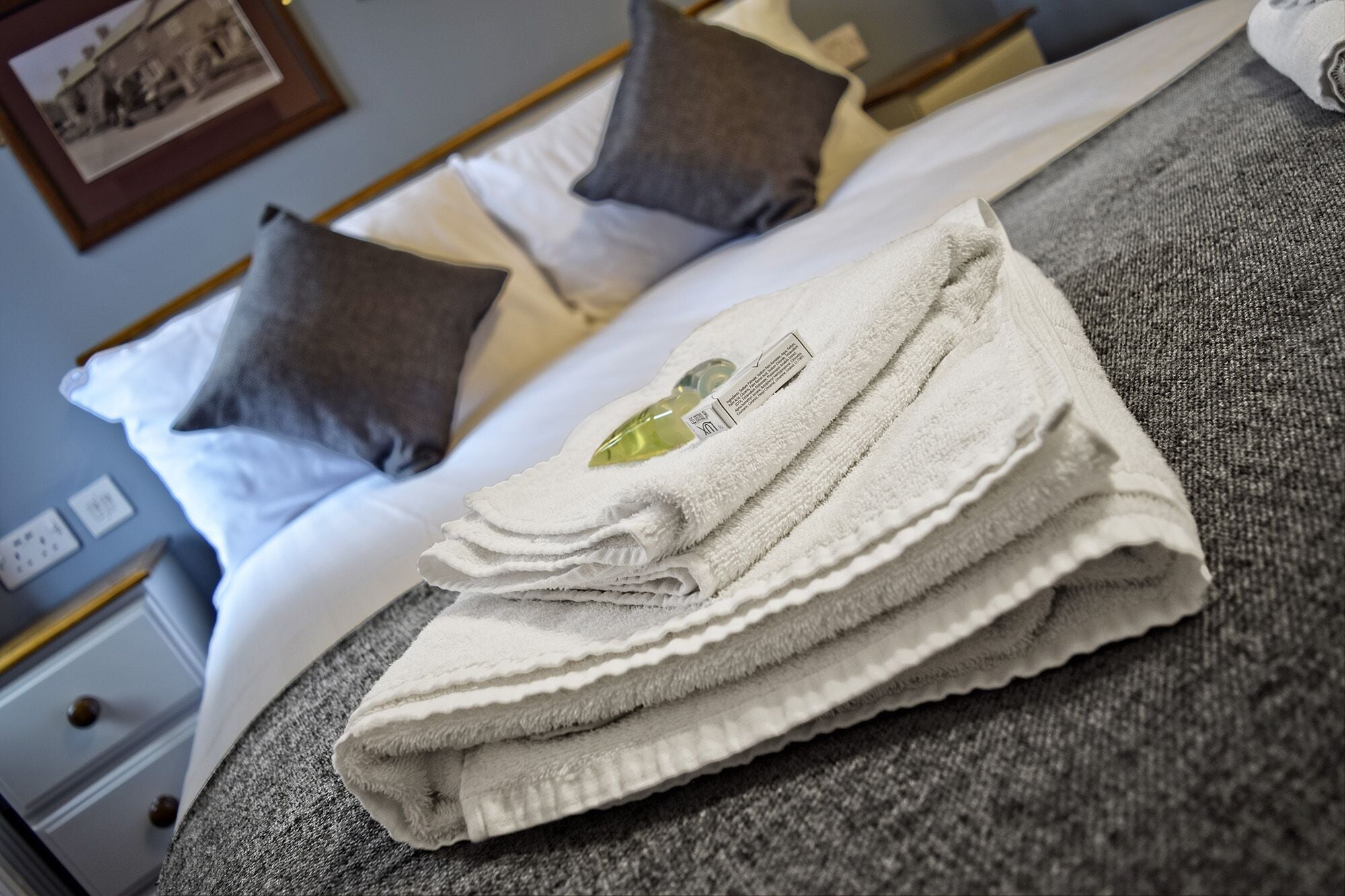A neatly made bed with white linens and a folded towel with a label on it.