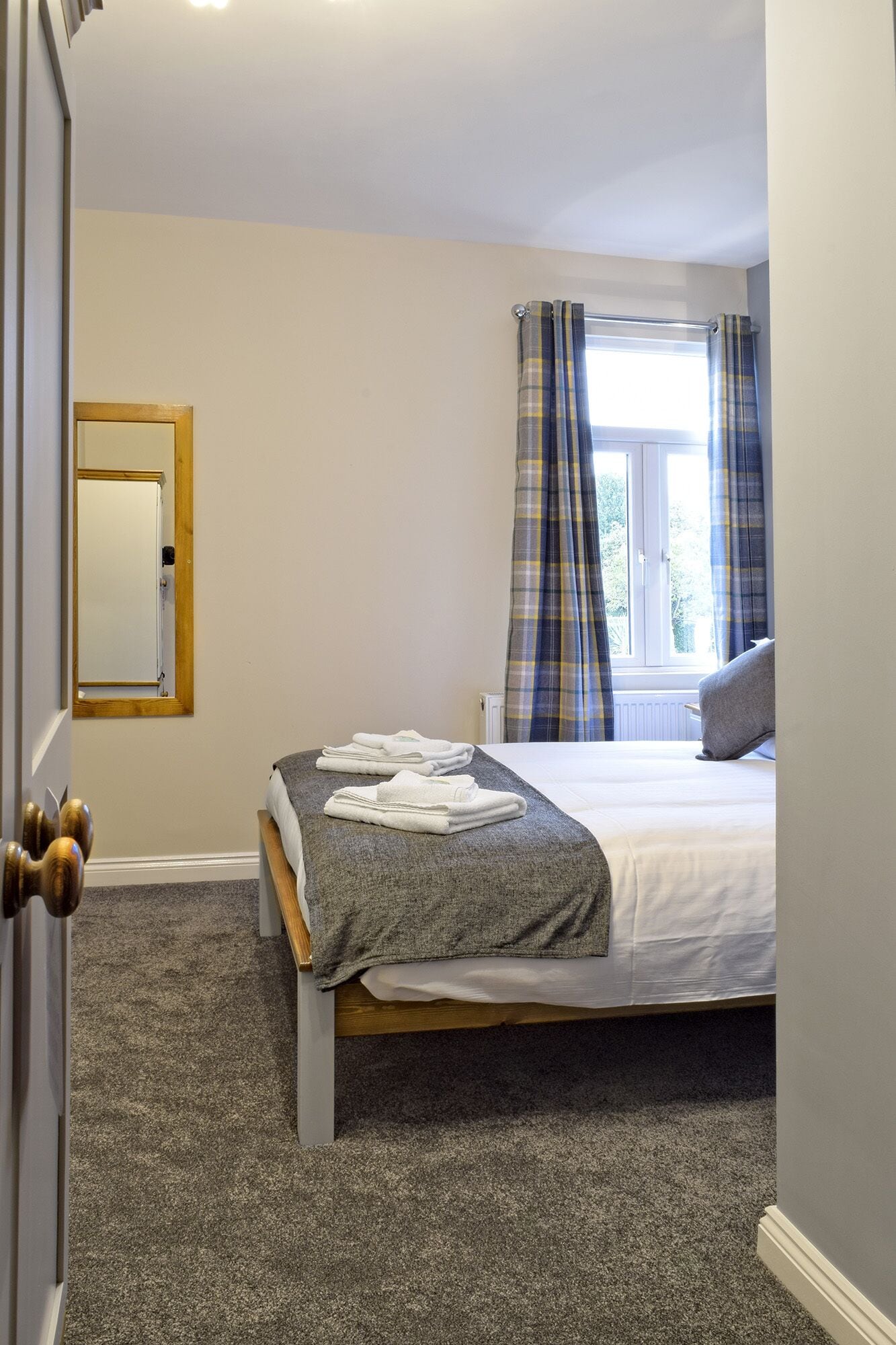 A bedroom with a bed, a window with curtains, a mirror, and a door.