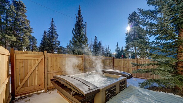 Ein Whirlpool in einem verschneiten Garten mit einer Holzterrasse und einem Holzzaun.