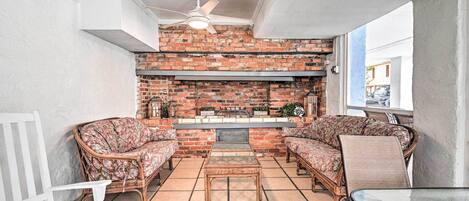 A cozy indoor seating area with wicker furniture, a brick wall, and a ceiling fan.