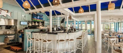 Ein Restaurant mit Barbereich, weißen Korbstühlen und einer blau-weißen Farbgestaltung.