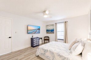 Un dormitorio con una cama, ventilador de techo, televisor, cómoda y una silla.