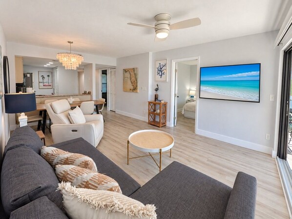 A modern living room with a sofa, coffee table, and a television displaying a beach scene.