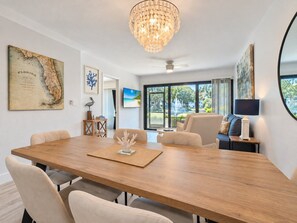 A spacious room with a large wooden table, comfortable seating, a chandelier, and artwork on the walls.