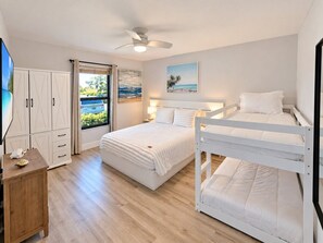 A bedroom with a bunk bed, a desk with a chair, a wardrobe, and a window with a view of the outdoors.