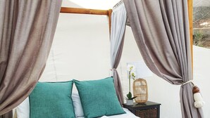 A bed with a white and teal color scheme, a wooden bench, and a wicker side table with a plant. - Africa's first Bubble Acomidation  (Piet Retief)