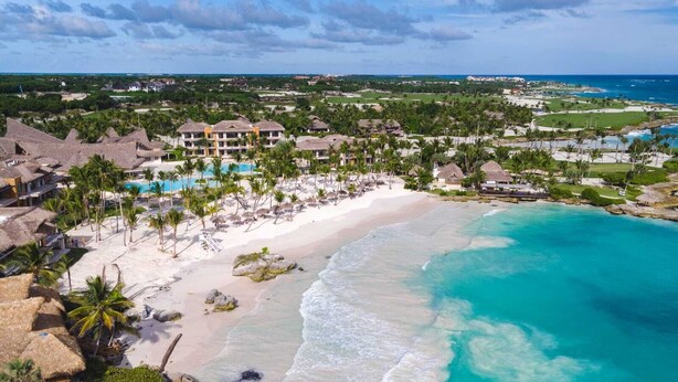 A resort with a beach, a pool, and thatched-roof buildings.