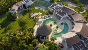 An aerial view of a resort with a tennis court, a swimming pool, and multiple buildings with solar panels.