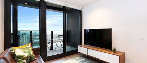 A modern living room with a leather sofa, a flat-screen TV, and a large window offering a city view.