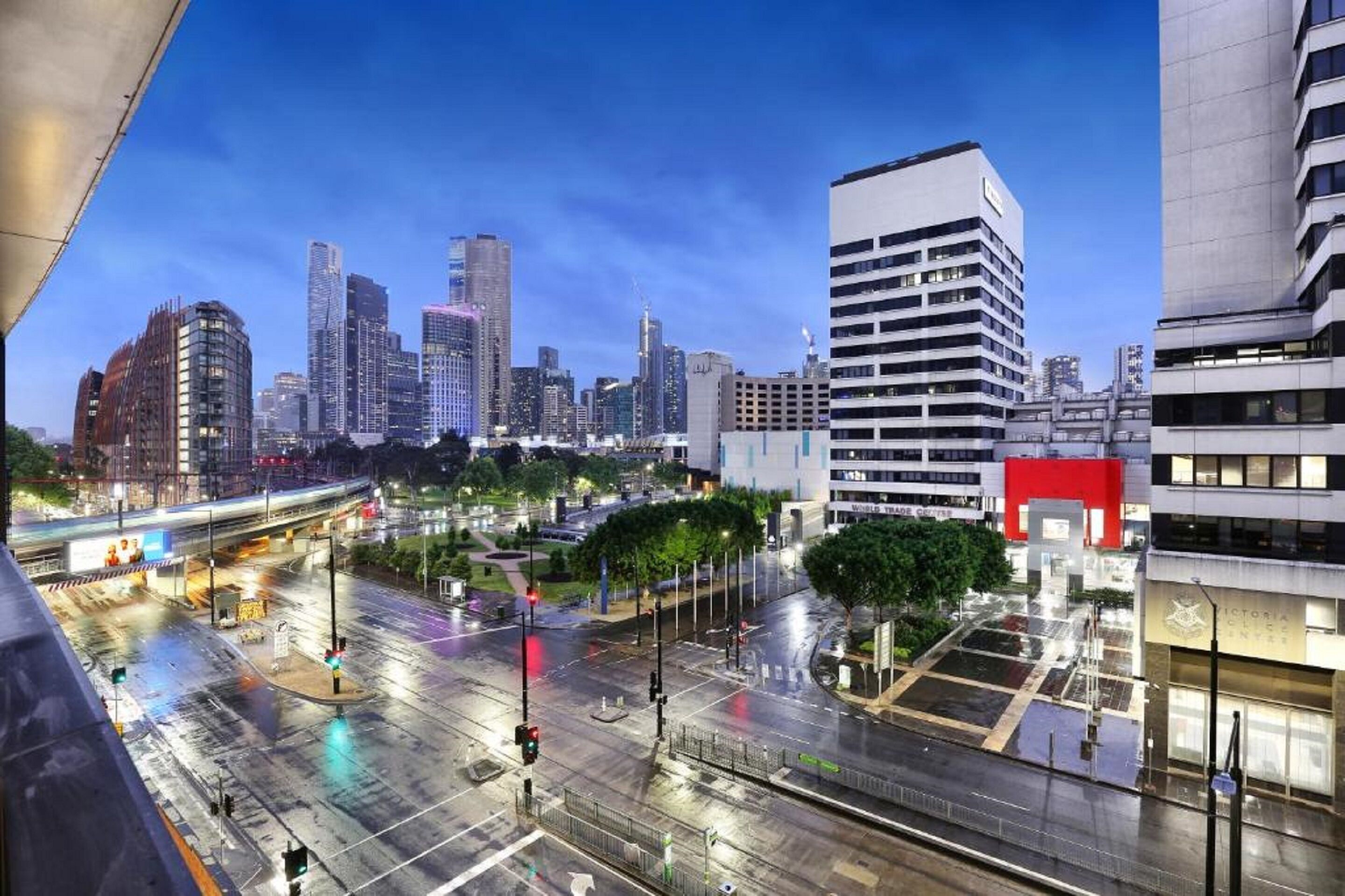 A cityscape with modern buildings, a prominent white building with a red section, and a well-lit intersection.