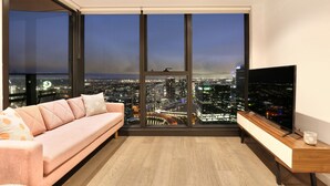 Ein modernes Wohnzimmer mit großem Fenster und Blick auf die Stadt, einem rosafarbenen Sofa, einem Holz-TV-Schrank und einem minimalistischen Einrichtungsstil.