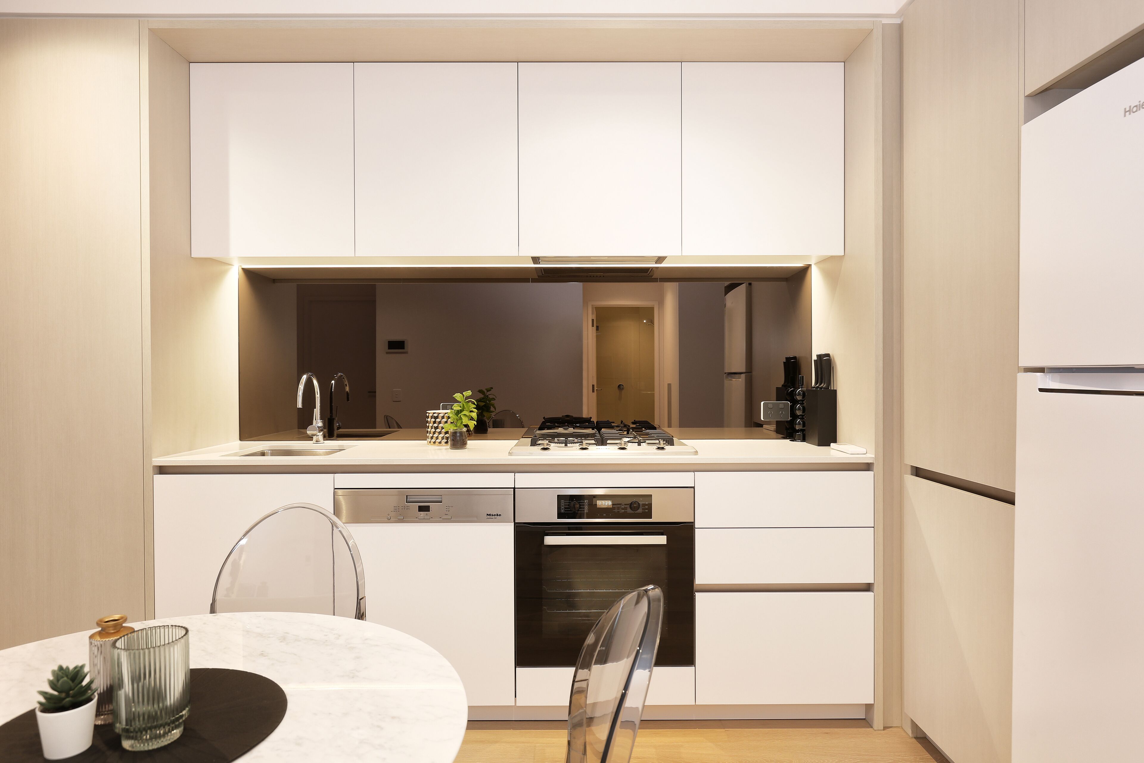 Cozinha moderna com armários brancos, lava-louças, forno e área de refeições com mesa e cadeiras.