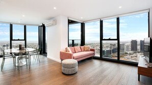 Ein großzügiger Wohnbereich mit einem großen Fenster, einem rosa Sofa, einem runden Esstisch und Holzboden.