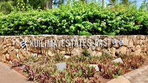 Un mur de pierre sur lequel on peut lire l’inscription « Kuilima Estates East » et qui est orné d’un logo, le tout étant entouré d’une végétation luxuriante.