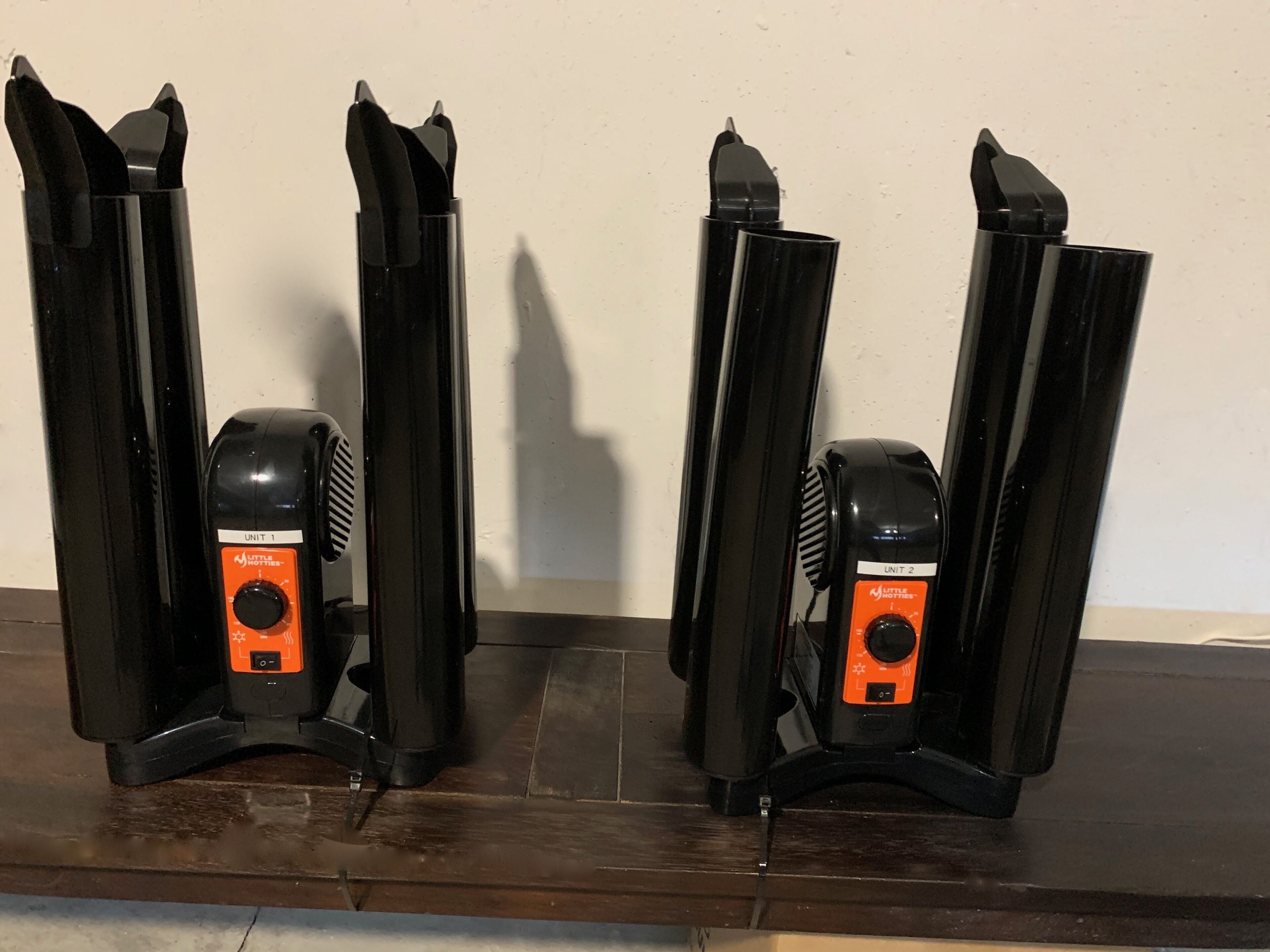 Two black speakers with orange accents, labeled "UNIT 1" and "UNIT 2," mounted on a dark wooden surface against a plain wall.