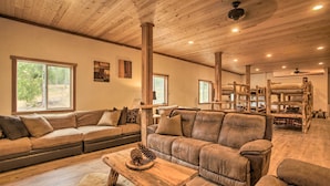 A spacious living room with a large sectional sofa, wooden flooring, and a high ceiling with exposed beams. - Rural Kettle Falls Bunkhouse w/ Airstrip & Trails! (Kettle Falls)
