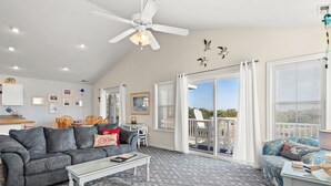 Un salon spacieux avec un canapé gris, une table basse et un balcon doté de balustrades blanches, offrant une vue sur le ciel.