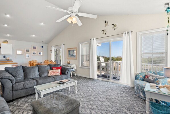 A spacious living room with a gray sofa, a coffee table, and a balcony with white railings and a view of the sky.
