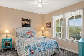 A bedroom with a bed, two bedside tables with lamps, a ceiling fan, and a window with blinds.