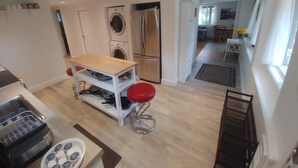 A modern kitchen with a built-in washing machine, a stainless steel refrigerator, and a wooden table with red bar stools. - Dominion Brook Park Vacation Rental - Beautiful suite with garden / park views. (North Saanich)