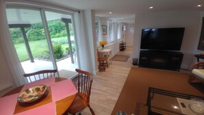 A spacious living area with a dining table, chairs, a TV, and a view of a garden. - Dominion Brook Park Vacation Rental - Beautiful suite with garden / park views. (North Saanich)
