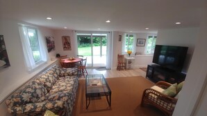 A living room with a sofa, coffee table, TV, and a dining area with chairs and a table. - Dominion Brook Park Vacation Rental - Beautiful suite with garden / park views. (North Saanich)