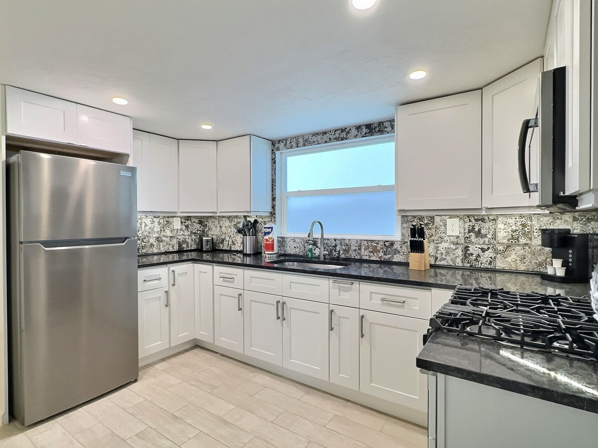 A modern kitchen with white cabinets, a stainless steel refrigerator, a gas stove, and a window above the sink.