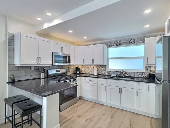 A modern kitchen with white cabinets, a black countertop, stainless steel appliances, and a wooden floor.