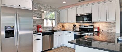 A modern kitchen with stainless steel appliances, white cabinetry, and a wooden floor.