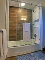 A glass-enclosed walk-in shower with a white bathtub, a towel rack, and a blue patterned rug.