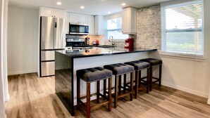 Een moderne keuken met roestvrijstalen apparatuur, een centraal eiland met barkrukken en een raam met jaloezieën.