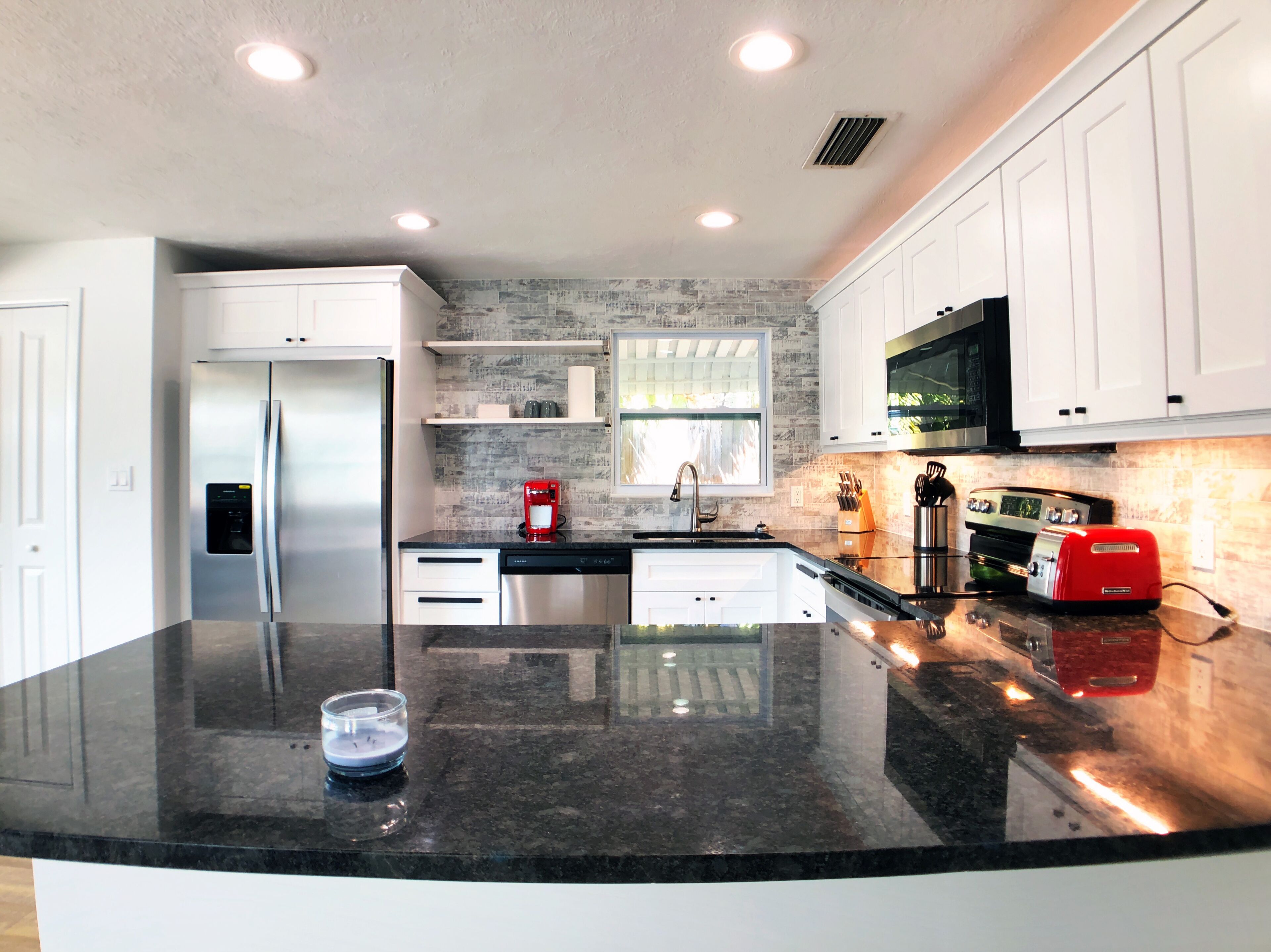 A modern kitchen with white cabinets, a stainless steel refrigerator, a red coffee maker, and a red toaster.