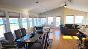 A spacious living area with a large dining table, comfortable seating, and a view of the beach through large windows. - Luxurious Beachfront House - spectacular ocean views - w/ indoor elevator (Old Orchard Beach)