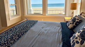 A bedroom with a view of the beach, a bed with patterned bedding, and a nightstand with a lamp. - Luxurious Beachfront House - spectacular ocean views - w/ indoor elevator (Old Orchard Beach)