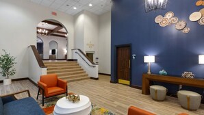 A hotel lobby with a staircase, orange seating, a round coffee table, and a blue wall with decorative plates. - Wyndham La Cascada, San Antonio 1 Bedroom Condo (San Antonio)