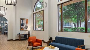 A modern interior with a blue sofa, orange chairs, a round white table, and large windows with a view of trees. - Wyndham La Cascada, San Antonio 1 Bedroom Condo (San Antonio)